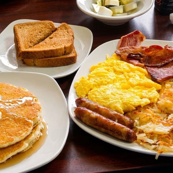 A hearty breakfast spread with pancakes, scrambled eggs, bacon, sausage, hash browns, and toast.
