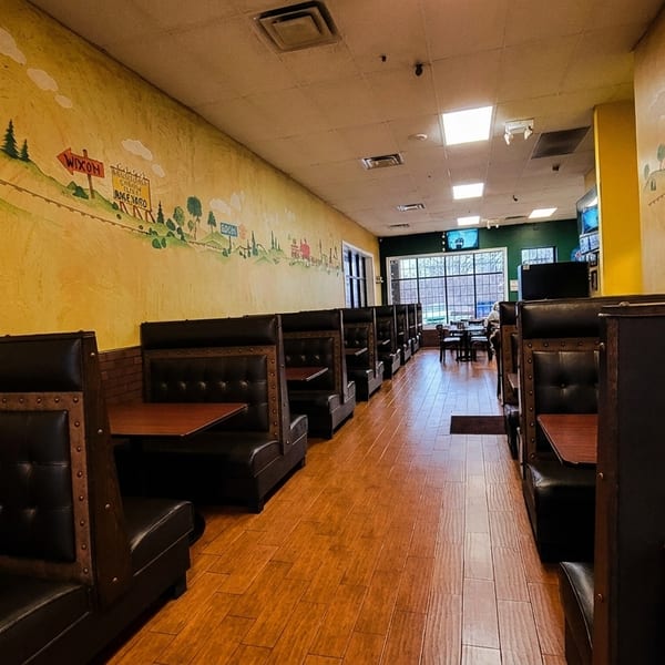 Restaurant interior with rows of dark leather booths, wooden tables, and a colorful mural on the wall.