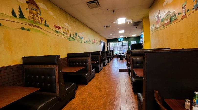 Restaurant interior with rows of dark leather booths, wooden tables, and a colorful mural on the wall.